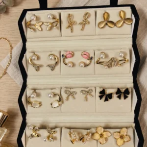 Curated 12-pair gold and pearl fashion earring collection displayed in an open black velvet four-tier jewelry travel organizer roll