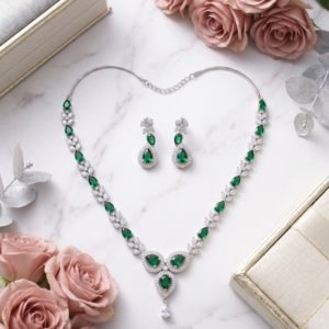 Elegant emerald green gemstone necklace and matching earrings displayed on a jewelry bust with a luxurious beige background.