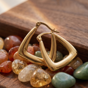 Geometric gold hoop earrings by Manadh Jewels crafted from premium stainless steel with a polished gold finish, displayed on a marble pedestal alongside a model wearing the earrings in a luxury setting