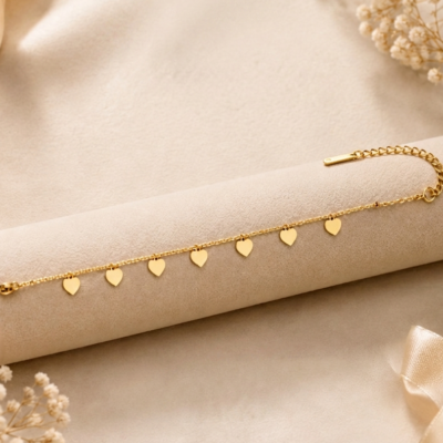 Gold heart charm bracelet by Manadh Jewels featuring multiple polished heart pendants on an adjustable stainless steel chain with a premium gold finish, displayed on an elegant marble backdrop.