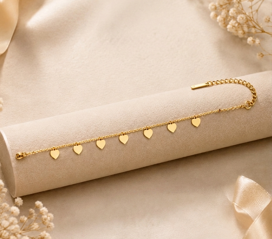 Gold Heart Charm Bracelet MND-BR007 Slide1 Gold heart charm bracelet by Manadh Jewels featuring multiple polished heart pendants on an adjustable stainless steel chain with a premium gold finish, displayed on an elegant marble backdrop.