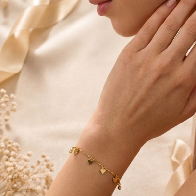 Gold heart charm bracelet by Manadh Jewels featuring multiple polished heart pendants on an adjustable stainless steel chain with a premium gold finish, displayed on an elegant marble backdrop.