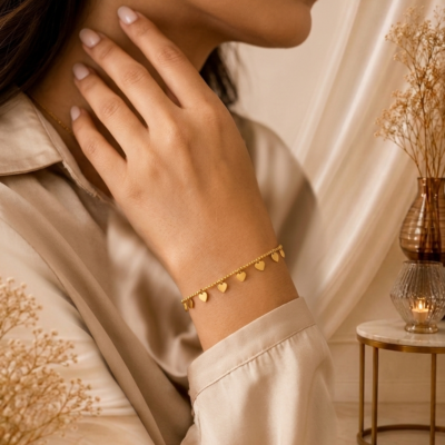 Gold heart charm bracelet by Manadh Jewels featuring multiple polished heart pendants on an adjustable stainless steel chain with a premium gold finish, displayed on an elegant marble backdrop.