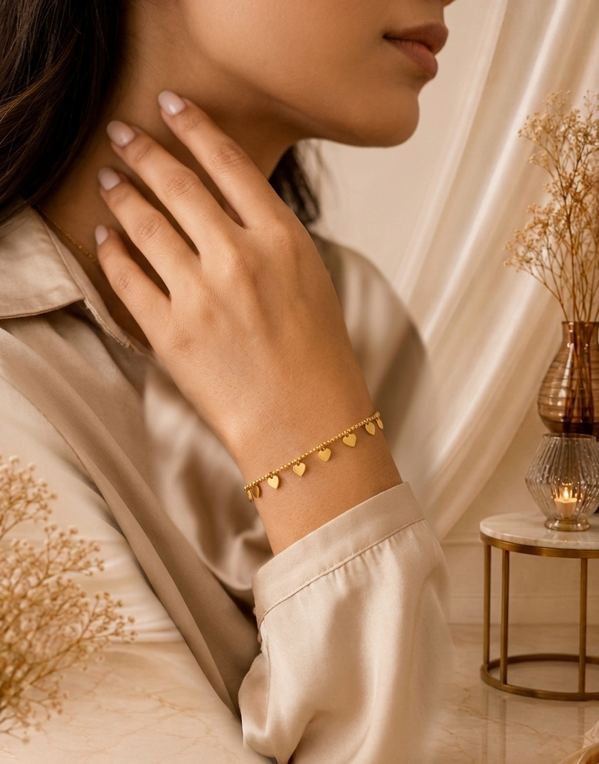 Gold Heart Charm Bracelet MND-BR007 Slide3 Gold heart charm bracelet by Manadh Jewels featuring multiple polished heart pendants on an adjustable stainless steel chain with a premium gold finish, displayed on an elegant marble backdrop.