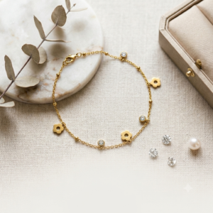 Elegant gold plated floral charm bracelet by Manadh Jewels featuring polished flower charms, crystal accents, black enamel detailing, and delicate dangling beads displayed on a premium jewelry stand.