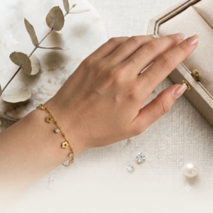 Elegant gold plated floral charm bracelet by Manadh Jewels featuring polished flower charms, crystal accents, black enamel detailing, and delicate dangling beads displayed on a premium jewelry stand.