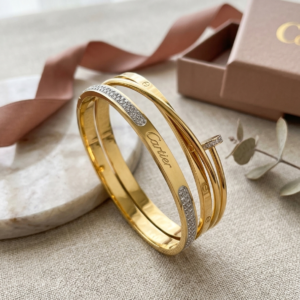 Gold-tone layered statement bangle with sparkling accent detailing on a wooden luxury jewellery display