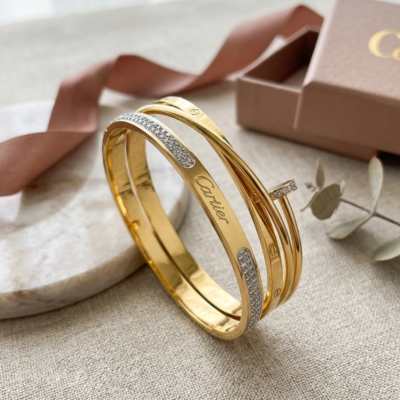 Gold-tone layered statement bangle with sparkling accent detailing on a wooden luxury jewellery display