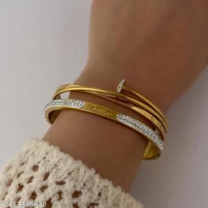 Gold-tone layered statement bangle with sparkling accent detailing on a wooden luxury jewellery display