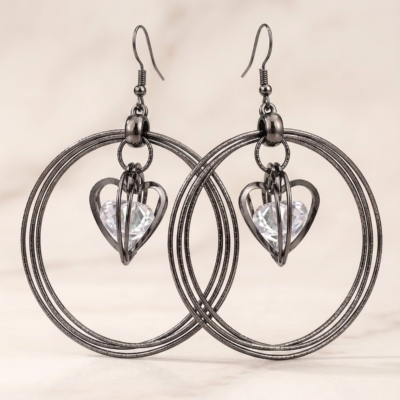 Elegant black hoop earrings featuring sparkling heart-shaped crystal charms displayed on a premium jewellery stand by MANADH JEWELS.