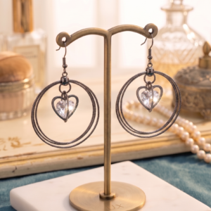 Elegant black hoop earrings featuring sparkling heart-shaped crystal charms displayed on a premium jewellery stand by MANADH JEWELS.