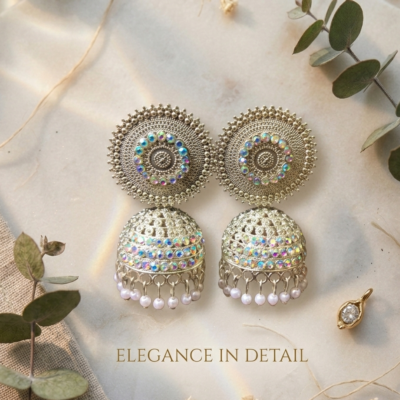 Premium oxidized jhumka earrings with intricate circular detailing, shimmering stones, and pearl drops displayed on a beige marble surface by Manadh Jewels