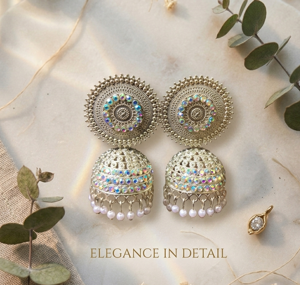 Oxidized Jhumka Earrings 1 Premium oxidized jhumka earrings with intricate circular detailing, shimmering stones, and pearl drops displayed on a beige marble surface by Manadh Jewels