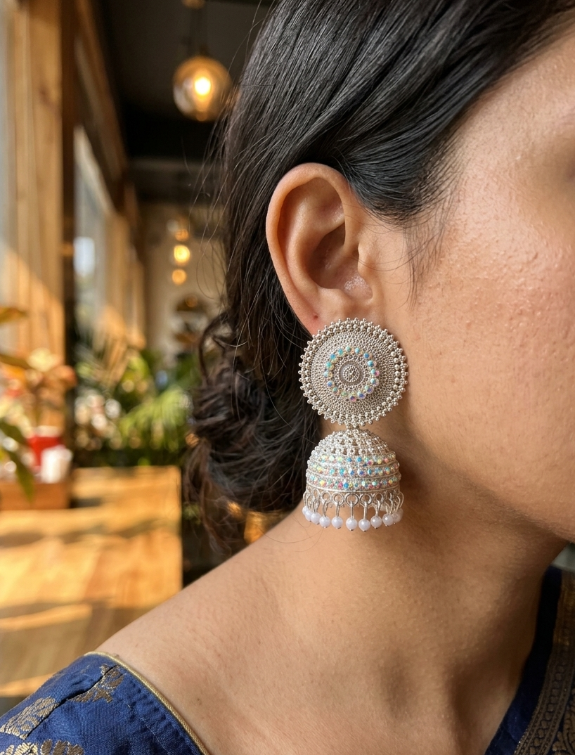 Oxidized Jhumka Earrings 2 Premium oxidized jhumka earrings with intricate circular detailing, shimmering stones, and pearl drops displayed on a beige marble surface by Manadh Jewels