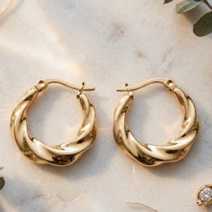 Twisted gold hoop earrings by Manadh Jewels crafted from premium stainless steel with a polished gold finish, displayed on a marble platform in an elegant luxury setting