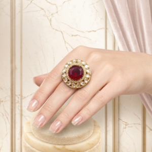 Luxury ruby statement ring by Manadh Jewels featuring a vibrant ruby-red center stone surrounded by sparkling halo accents in a premium gold-tone setting, displayed in 360-degree front, side, back, and angle views.