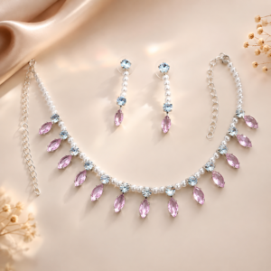 Elegant pink crystal and pearl necklace set with matching drop earrings on a soft satin background.