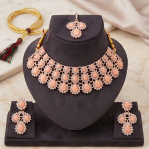 Manadh Jewels luxurious rose gold bridal choker necklace set featuring layered teardrop peach stones and sparkling crystals, complete with matching drop earrings and a coordinating maang tikka