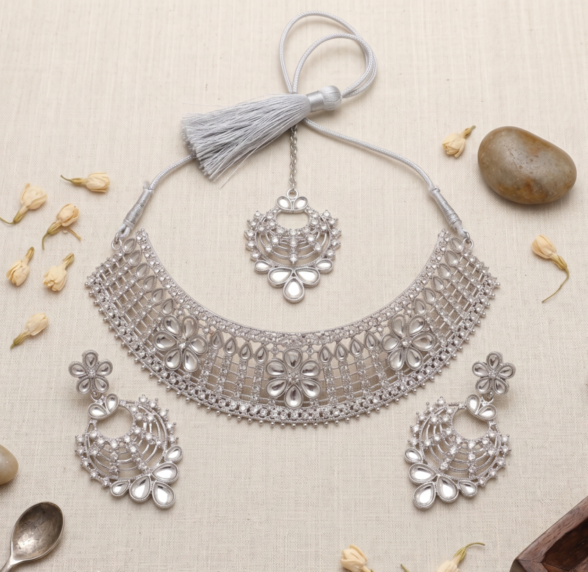Silver-Toned Floral Bridal Choker Set with Earrings & Tikka 1 Manadh Jewels silver-tone bridal choker necklace set featuring intricate floral motifs and clear crystal mirror-style stones, complete with matching drop earrings and a coordinating maang tikka