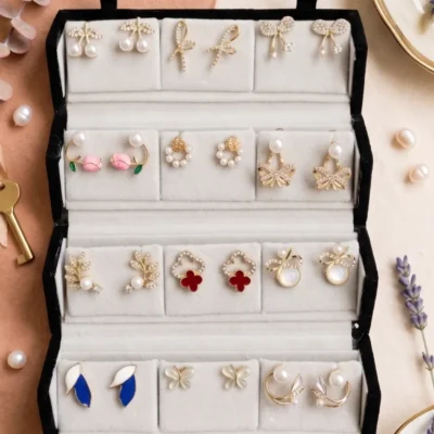 Curated 12-pair gold and pearl fashion earring collection displayed in an open black velvet four-tier jewelry travel organizer roll