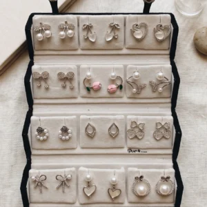 Curated 12-pair gold and pearl fashion earring collection displayed in an open black velvet four-tier jewelry travel organizer roll