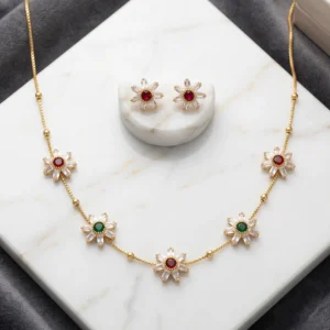Gold-tone necklace set featuring floral pendants with white, red, and green stones alongside matching stud earrings