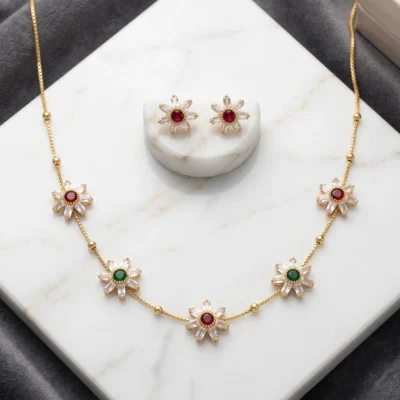 Gold-tone necklace set featuring floral pendants with white, red, and green stones alongside matching stud earrings