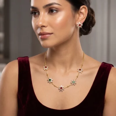 Gold-tone necklace set featuring floral pendants with white, red, and green stones alongside matching stud earrings