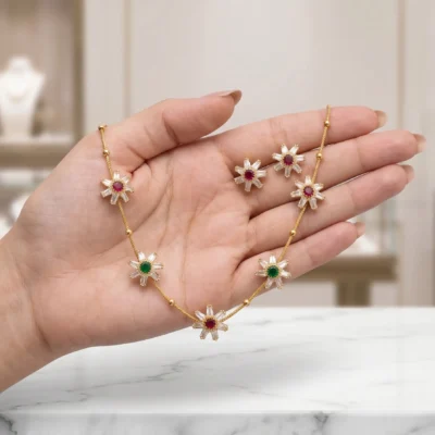 Gold-tone necklace set featuring floral pendants with white, red, and green stones alongside matching stud earrings