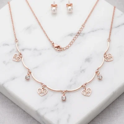 Rose gold-tone necklace with heart charms reading LOVE and YOU alongside pearl stud earrings