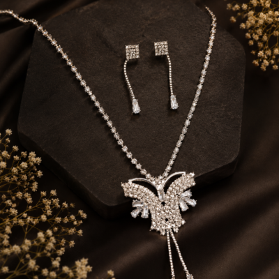 Silver-tone crystal butterfly pendant necklace with matching rhinestone drop earrings held in a hand