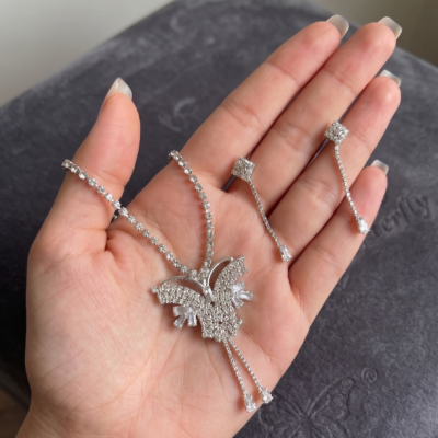 Silver-tone crystal butterfly pendant necklace with matching rhinestone drop earrings held in a hand