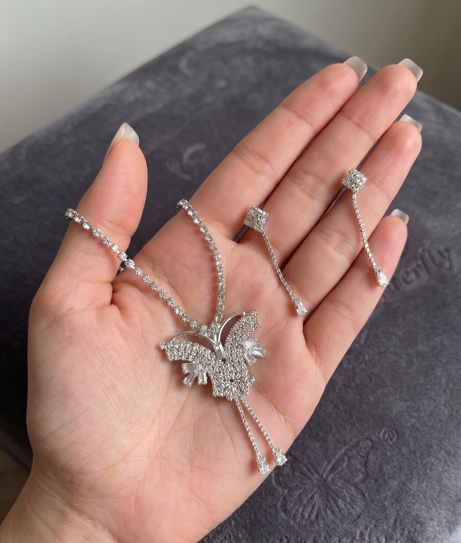 Silver Crystal Butterfly Necklace &_ Earring Set 3 Silver-tone crystal butterfly pendant necklace with matching rhinestone drop earrings held in a hand